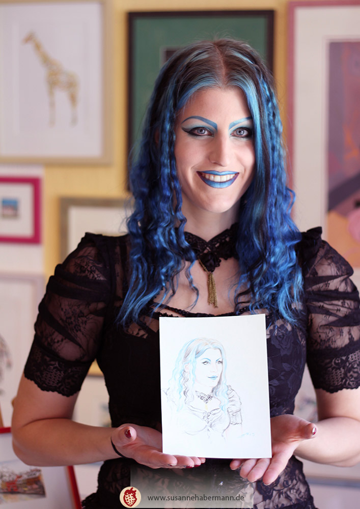 Porträtzeichnen - junge Frau mit blauen Haaren und Gothic-Outfit freut sich über ihr Portrait - Porträtzeichnen auf Veranstaltungen mit Susanne Habermann